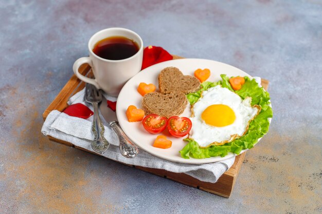 Free photo breakfast on valentine's day - fried eggs and bread in the shape of a heart and fresh vegetables.