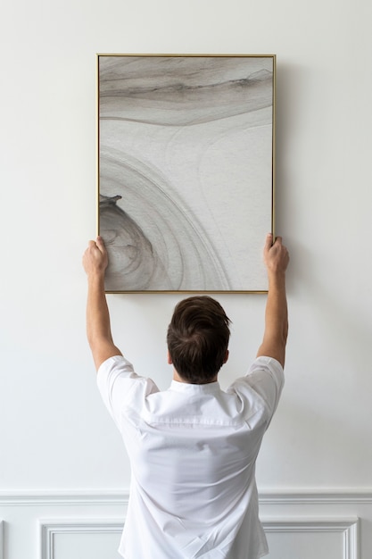 Bezpłatne zdjęcie abstrakcyjny obraz powieszony przez młodego mężczyznę na białej minimalnej ścianie