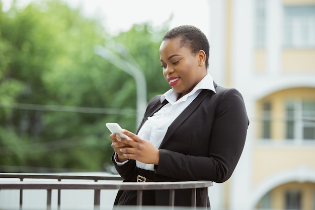 African American businesswoman w stroju biurowym uśmiechnięty, wygląda pewnie i szczęśliwy, zajęty