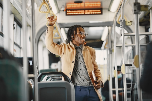 African American człowiek jedzie w autobusie miejskim. Facet w brązowym płaszczu. Człowiek z notatnikiem.