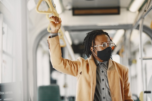 African American człowiek jedzie w autobusie miejskim. Facet w brązowym płaszczu. Koncepcja wirusa koronowego.