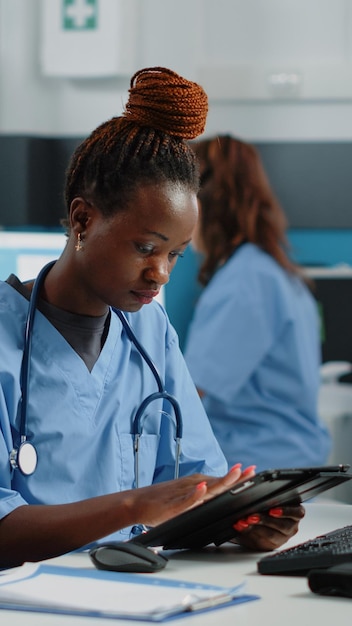 African American Pielęgniarka Trzymając Tablet Cyfrowy Na Wizytę Kontrolną W Gabinecie Lekarzy. Czarna Kobieta Pracuje Jako Asystent Medyczny, Używając Urządzenia Z Ekranem Dotykowym Do Opieki Zdrowotnej I Medycyny.