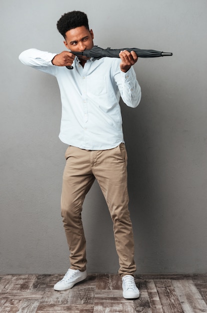 Bezpłatne zdjęcie afro amerykanin używa parasola jak pistolet i strzela