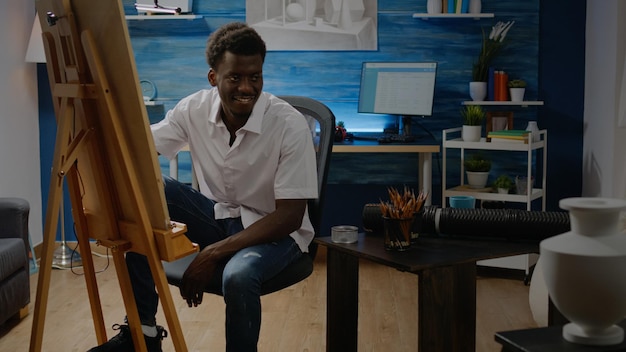 Afroamerykanin Dorosły Siedzi W Studiu Grafiki, Rysując Ołówkiem, Wazonem I Białym Płótnem Na Sztalugach. Czarny Młody Człowiek Z Kreatywnym Hobby Tworzącym Udane Arcydzieło I Dzieła Sztuki