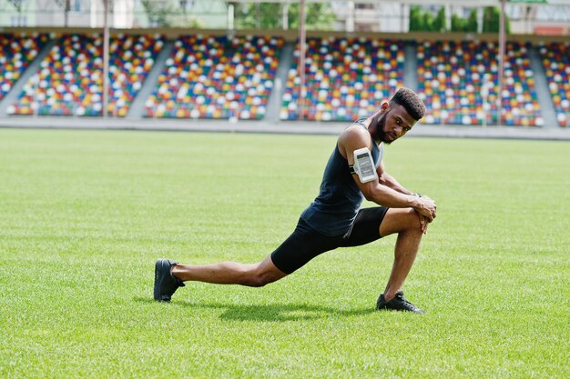 Afroamerykanin męski sportowiec w odzieży sportowej robi ćwiczenia rozciągające na stadionie