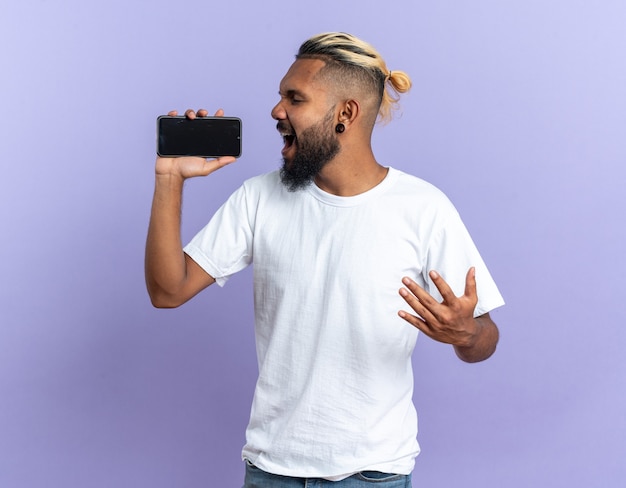 Afroamerykanin, Młody Człowiek W Białej Koszulce, Trzymający Smartfona, Używający Jako Mikrofonu śpiewającego Radośnie I Emocjonalnie