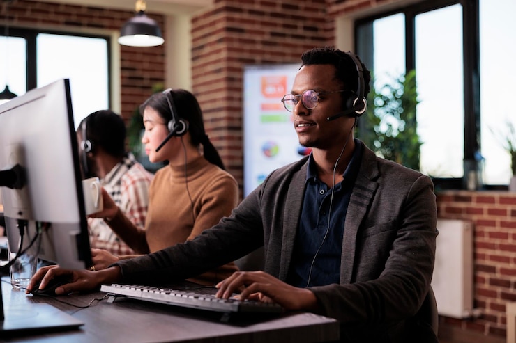 Bezpłatny plik Zdjęcie afroamerykanin pracownik infolinii pracujący w recepcji call center z wieloma monitorami. mężczyzna operator za pomocą telekomunikacji, aby pomóc klientom w obsłudze klienta, sieci zdalnej.