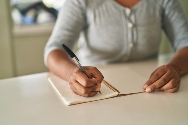 Afroamerykanka pisząca w notatniku siedzącym na stole w domu