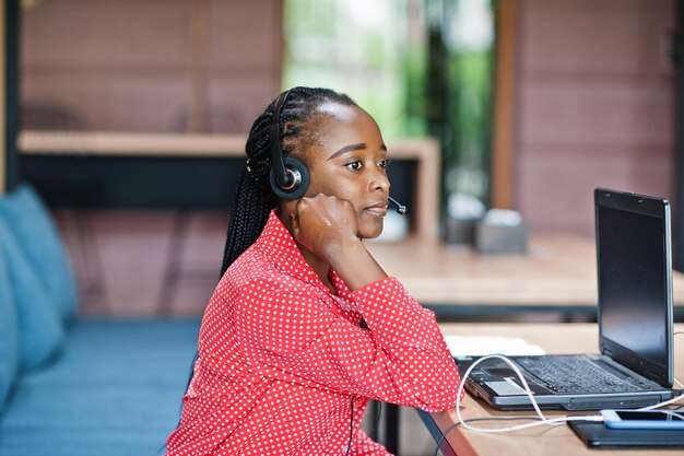 Afroamerykanka pracuje w call center operatora i agenta obsługi klienta, nosząc słuchawki z mikrofonem, pracując na laptopie