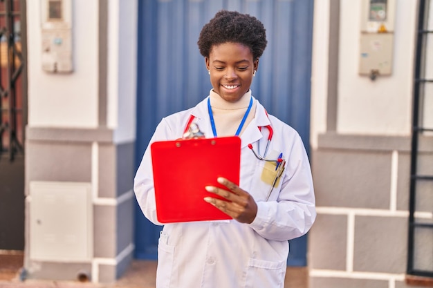 Bezpłatne zdjęcie afroamerykanka ubrana w mundur lekarza pisząca w schowku na ulicy