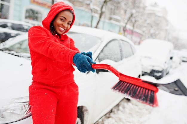 Afroamerykanka w czerwonej bluzie z kapturem czysty samochód od śniegu w zimowy dzień