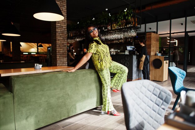 Afroamerykanka w stylu glamour nosi modną wężową sukienkę i okulary przeciwsłoneczne w restauracji