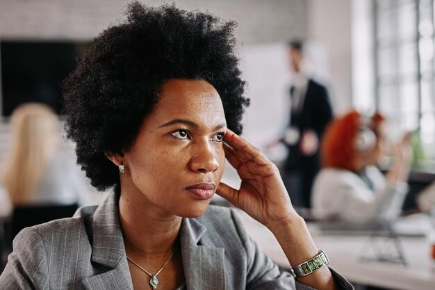 Afroamerykańska bizneswoman wyglądająca na zamyśloną będąc w biurze W tle są ludzie