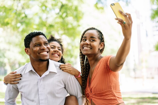 Afroamerykańska rodzina bawi się i cieszy dzień w parku, robiąc selfie razem z telefonem komórkowym.