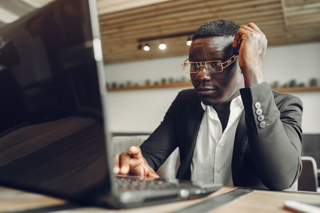 Afrykanin. Facet w czarnym garniturze. Mężczyzna z laptopem. Biznesmen w biurze.