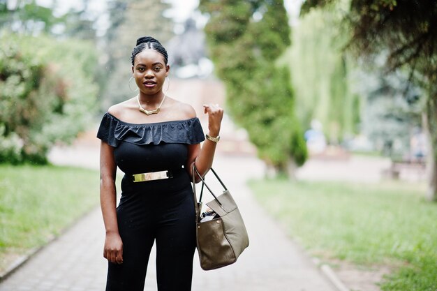Afrykańska dziewczyna pozuje na ulicy miasta, ubrana na czarno z torebką