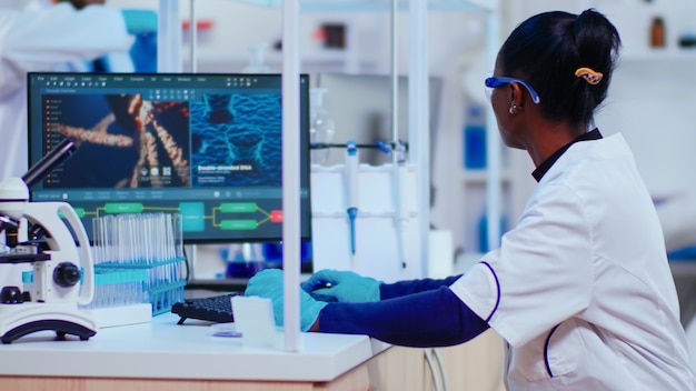 Afrykańska kobieta biochemik, badaczka sprawdzająca objawy szczepionki, pracująca w nowocześnie wyposażonym laboratorium. Wieloetniczni lekarze badający ewolucję wirusa za pomocą zaawansowanej technologicznie diagnostyki badawczej