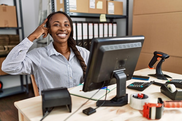 Afrykańska kobieta pracująca w małym biznesie e-commerce uśmiecha się, wskazując głową jednym palcem, świetny pomysł lub myśl, dobra pamięć