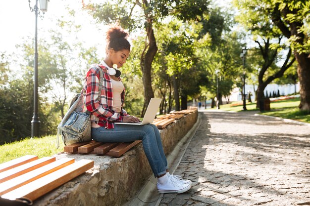 Afrykańska kobieta siedzi outdoors w parku używać laptop.