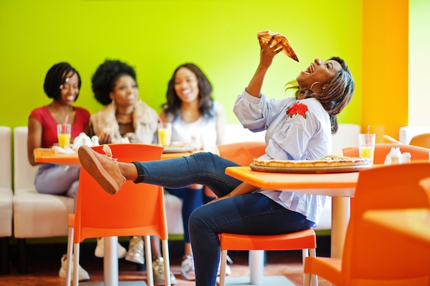 Afrykańska kobieta z pizzą siedząca w restauracji na tle ciemnoskórych dziewcząt