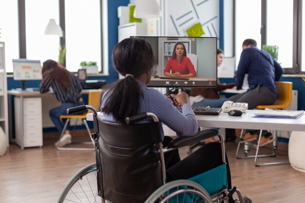 Afrykańska niepełnosprawna niepełnosprawna bizneswoman siedząca unieruchomiona na wózku inwalidzkim, rozmawiająca ze zdalnym partnerem podczas rozmowy wideo ze startowego biura biznesowego