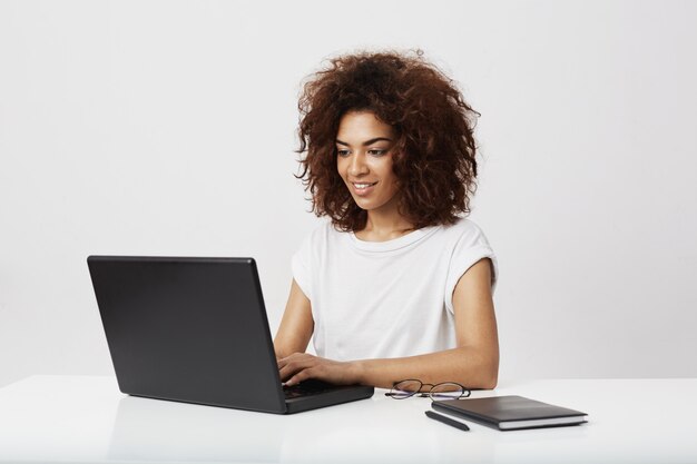 Afrykański bizneswoman uśmiecha się działanie przy laptopem nad biel ścianą.