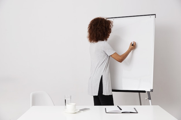 Afrykański dziewczyny writing stoi z powrotem blisko markiera whiteboard. Skopiuj miejsce