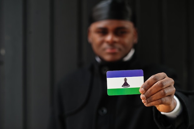 Bezpłatne zdjęcie afrykański mężczyzna nosi czarny durag trzymaj pod ręką flagę lesotho na białym tle ciemnego tła