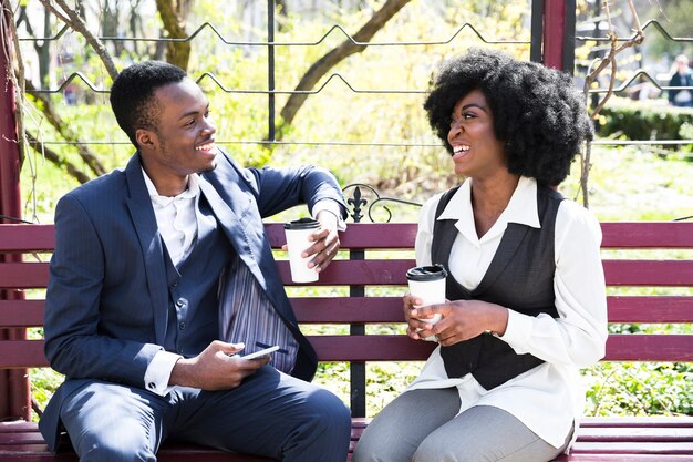 Afrykański młody biznesmen i bizneswoman siedzi na ławce trzyma jednorazową filiżankę kawy