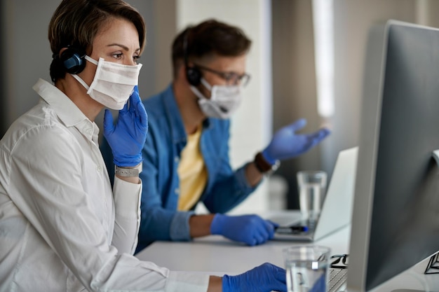 Agent call center noszący maskę ochronną podczas korzystania z komputera i pracy w biurze podczas epidemii wirusa