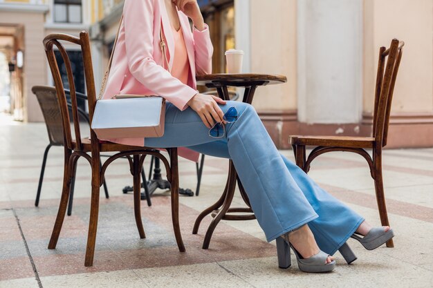 Akcesoria stylowej kobiety siedzącej w kawiarni, szczypce do spodni w stylu vintage, nogi w dżinsach, buty na obcasie, okulary przeciwsłoneczne, torebka, różowo-niebieskie kolory, wiosenno-letni trend w modzie, elegancki styl
