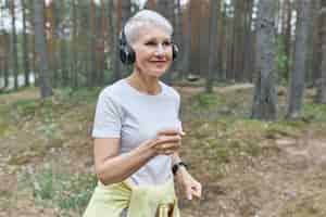Bezpłatne zdjęcie aktywna dojrzała kobieta biegacz w strojach sportowych i słuchawkach bezprzewodowych, słuchanie muzyki w słuchawkach.