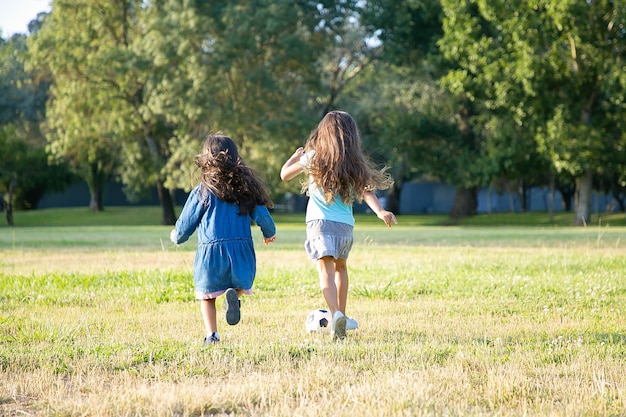 Aktywne czarne włosy dziewczyny biegają do piłki nożnej na trawie w parku miejskim. Pełna długość, widok z tyłu. Koncepcja dzieciństwa i aktywności na świeżym powietrzu
