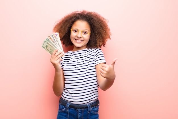 Amerykanin afrykańskiego pochodzenia mała dziewczynka przeciw płaskiej ścianie z dolarowymi banknotami