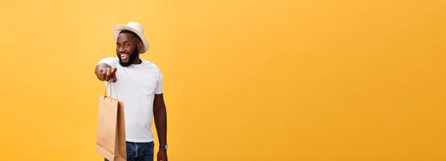 Amerykanin afrykańskiego pochodzenia mężczyzna z kolorowymi papierowymi torbami odizolowywać na żółtym tle