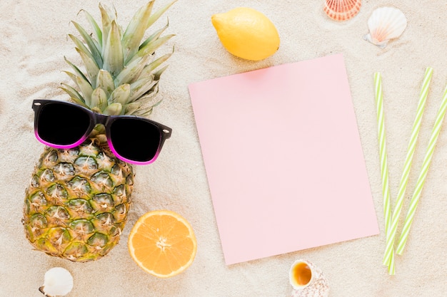Bezpłatne zdjęcie ananas z okularami przeciwsłonecznymi i papierem na piasku