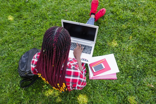 Anonimowy kobieta studiuje z komputerem na trawniku