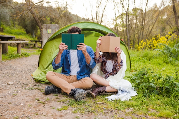Bezpłatne zdjęcie anonimowy para czytanie książek w pobliżu namiotu