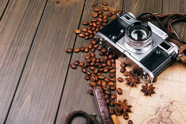 Aparat fotograficzny, ziarna kawy, cynamon i inne gatunki leżą na starej drewnianej mapie