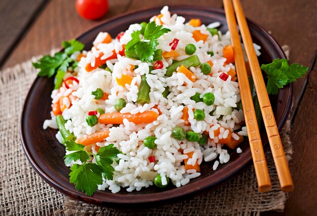 Apetyczny zdrowy ryż z warzywami w białym talerzu na drewnianym stole.