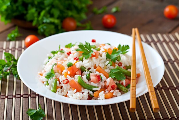 Apetyczny zdrowy ryż z warzywami w białym talerzu na drewnianym stole.