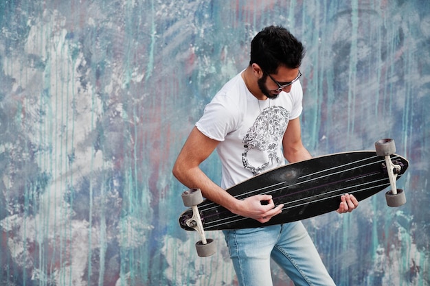 Arab W Stylu Ulicznym W Okularach Z Longboardem Ustawionym Na Kolorowej ścianie, Jakby Grał Na Gitarze