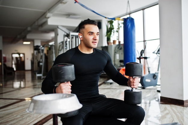 Arabski muskularny mężczyzna trening z hantlami w nowoczesnej siłowni.