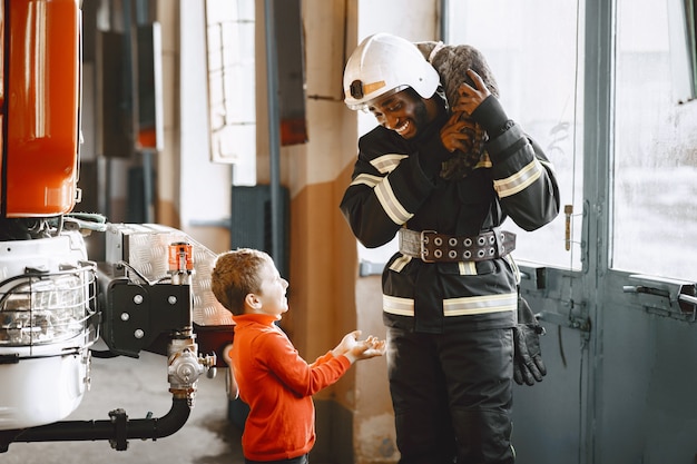 Bezpłatne zdjęcie arfican strażak w mundurze. człowiek przygotowuje się do pracy. facet z dzieckiem.