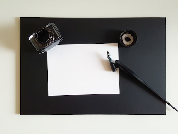 Arkusz papieru, długopis i tusz czarny na czarnym biurku.