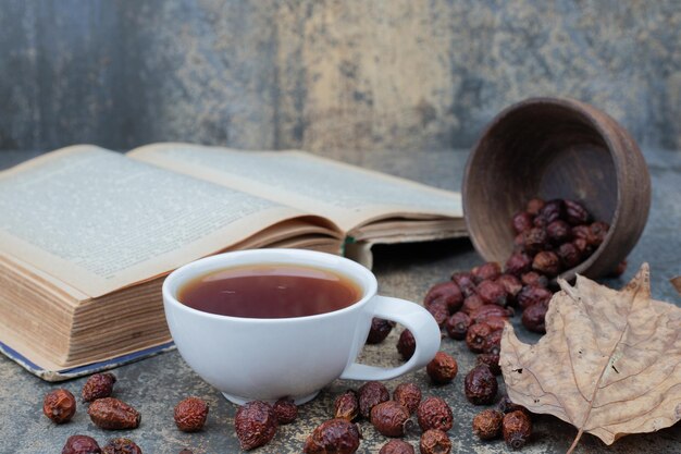 Aromatyczna herbata w białej filiżance z liściem i książką na marmurowym stole