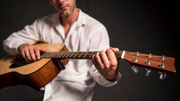 Artysta w białej koszuli gra na gitarze akustycznej w studio