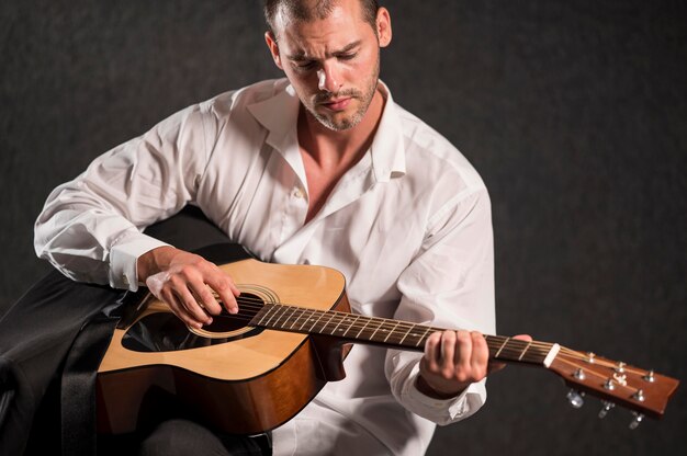 Artysta w białej koszuli siedzi i gra na gitarze
