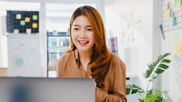 Asia businesswoman społeczne dystansowanie się w nowej normalnej sytuacji w celu zapobiegania wirusom podczas korzystania z prezentacji laptopa współpracownikom na temat planu rozmowy wideo podczas pracy w biurze.