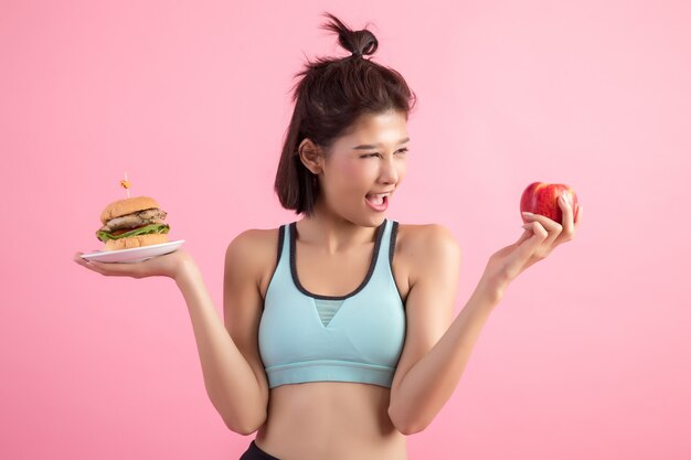 asian kobieta wybierając między hamburger i czerwone jabłko na różowo